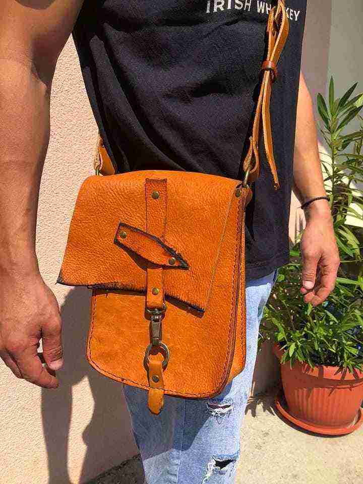 Čovek nosi kožnu tašnu narandžaste boje